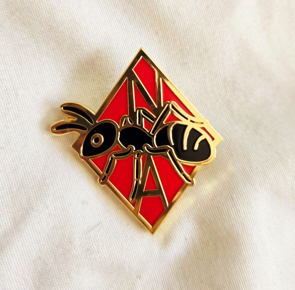 The Order of the Ant pin: a black ant over a red enamel N and A, edged in gold.